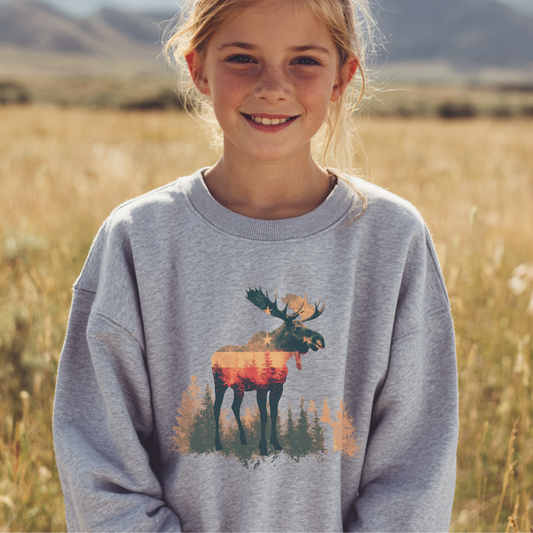 Young girl wearing a gray sweatshirt with a moose design in a field