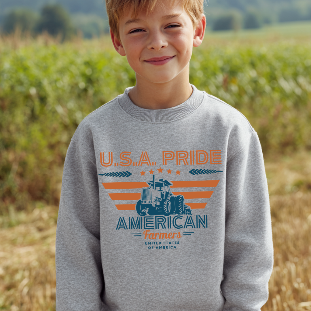 Child wearing a gray sweatshirt with 'U.S.A. Pride American Farmers' design in a field.