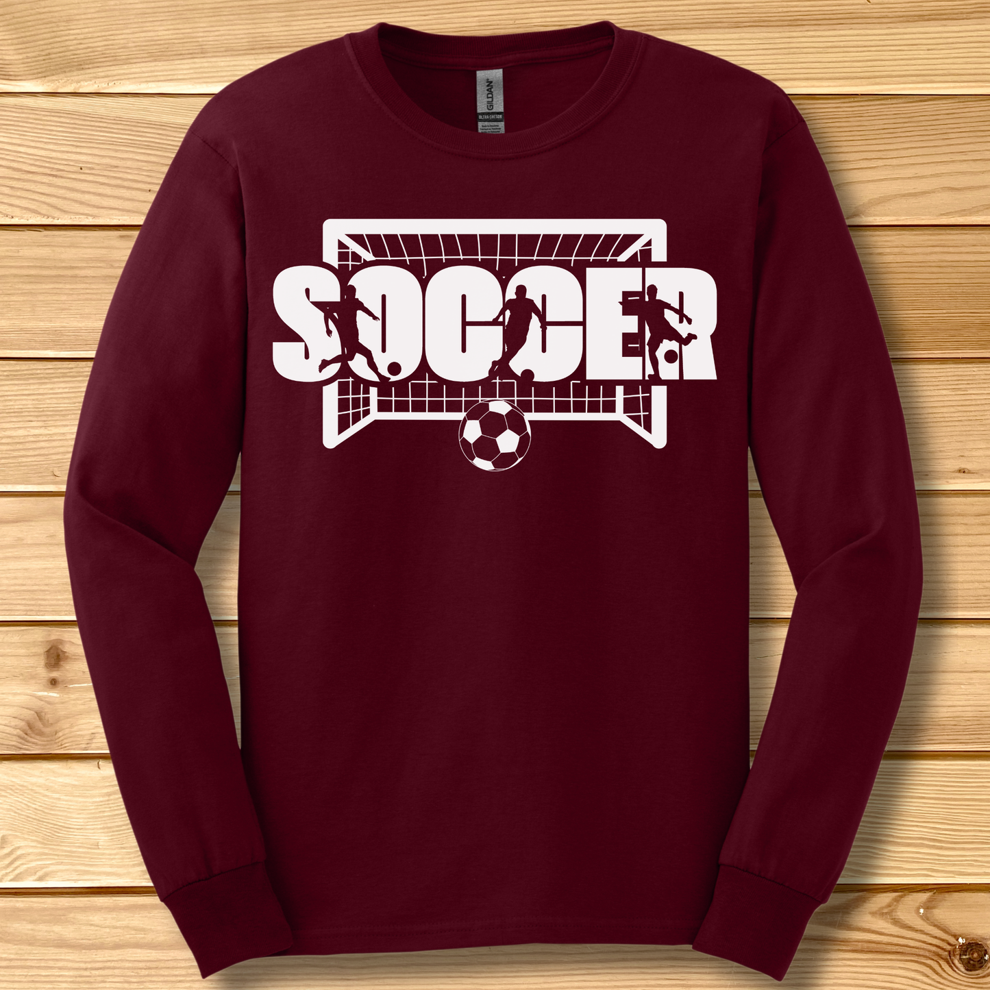 Maroon long-sleeve shirt with 'SOCCER' graphic on a wooden surface