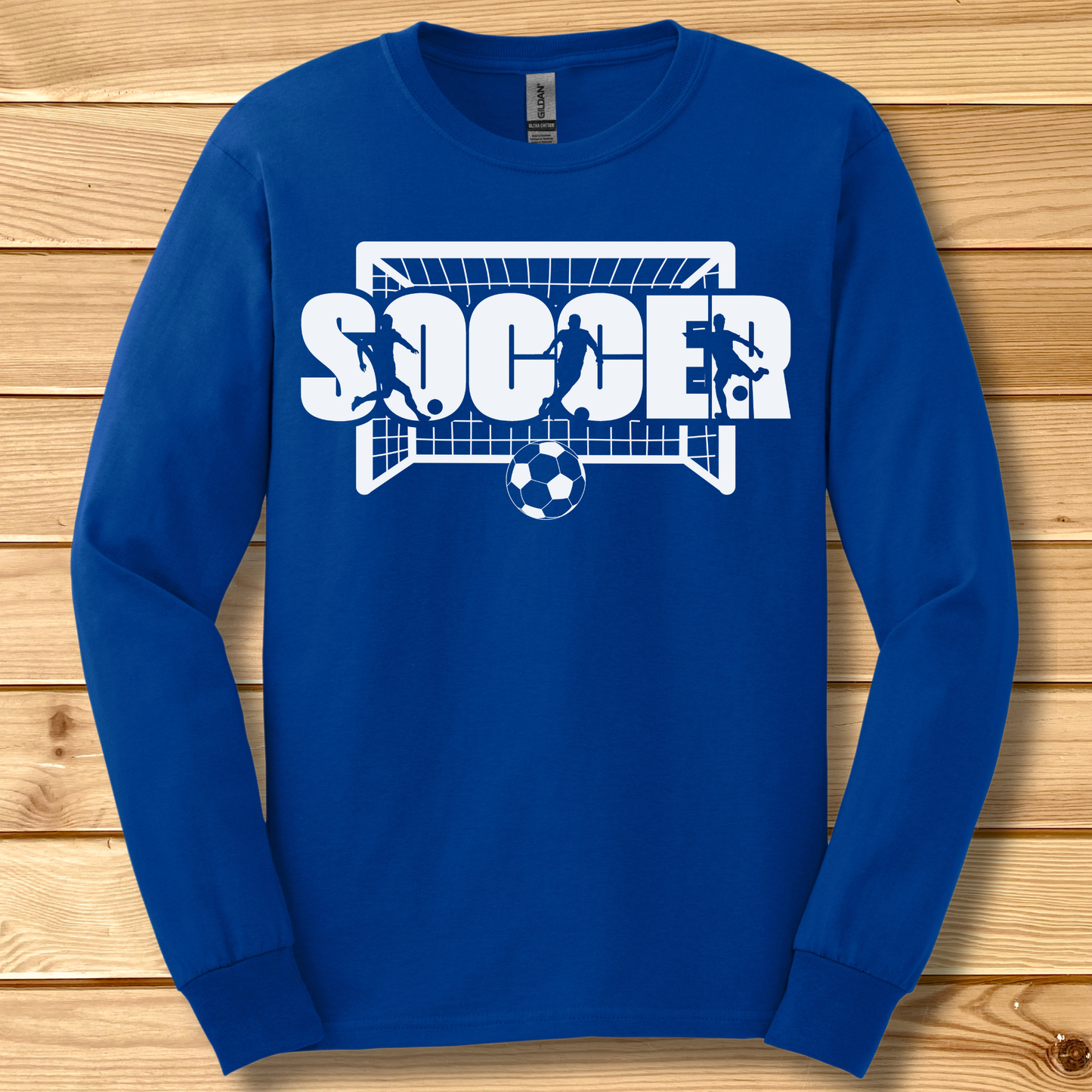Blue long-sleeve shirt with 'SOCCER' graphic on a wooden background