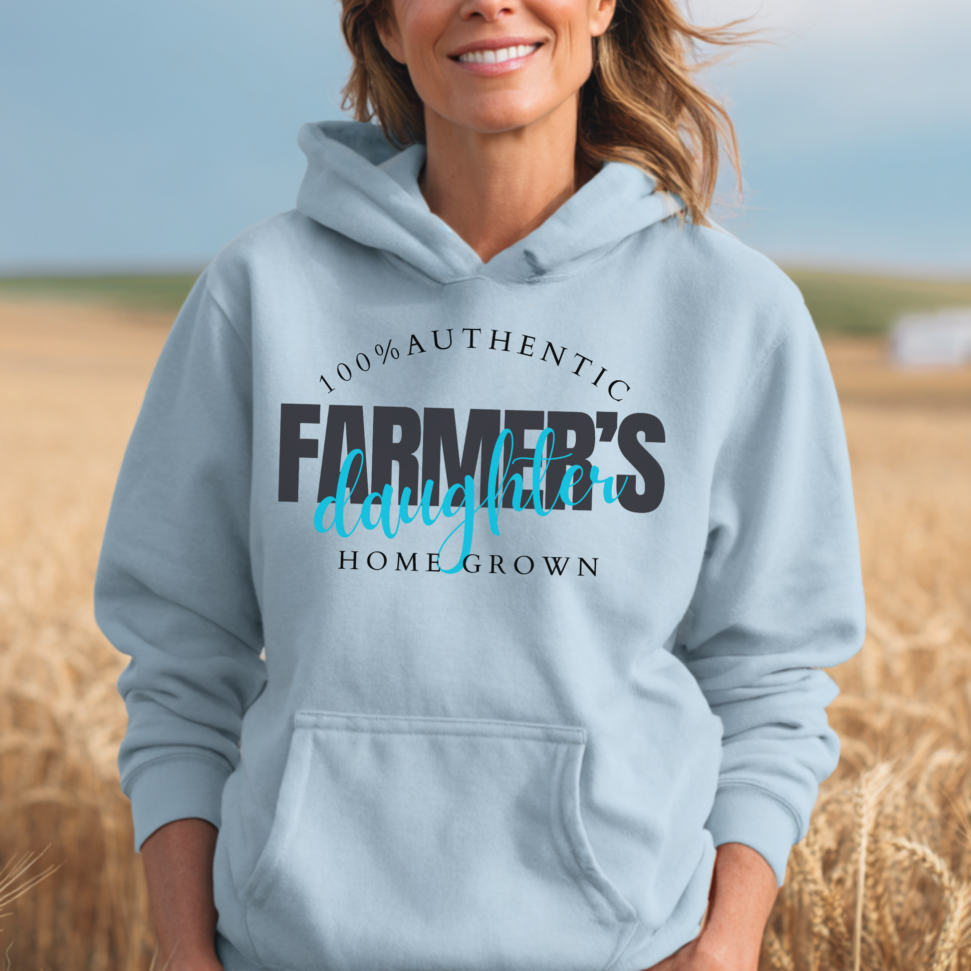 Person wearing a light blue hoodie with '100% Authentic Farmer's Daughter Home Grown' text in a field.