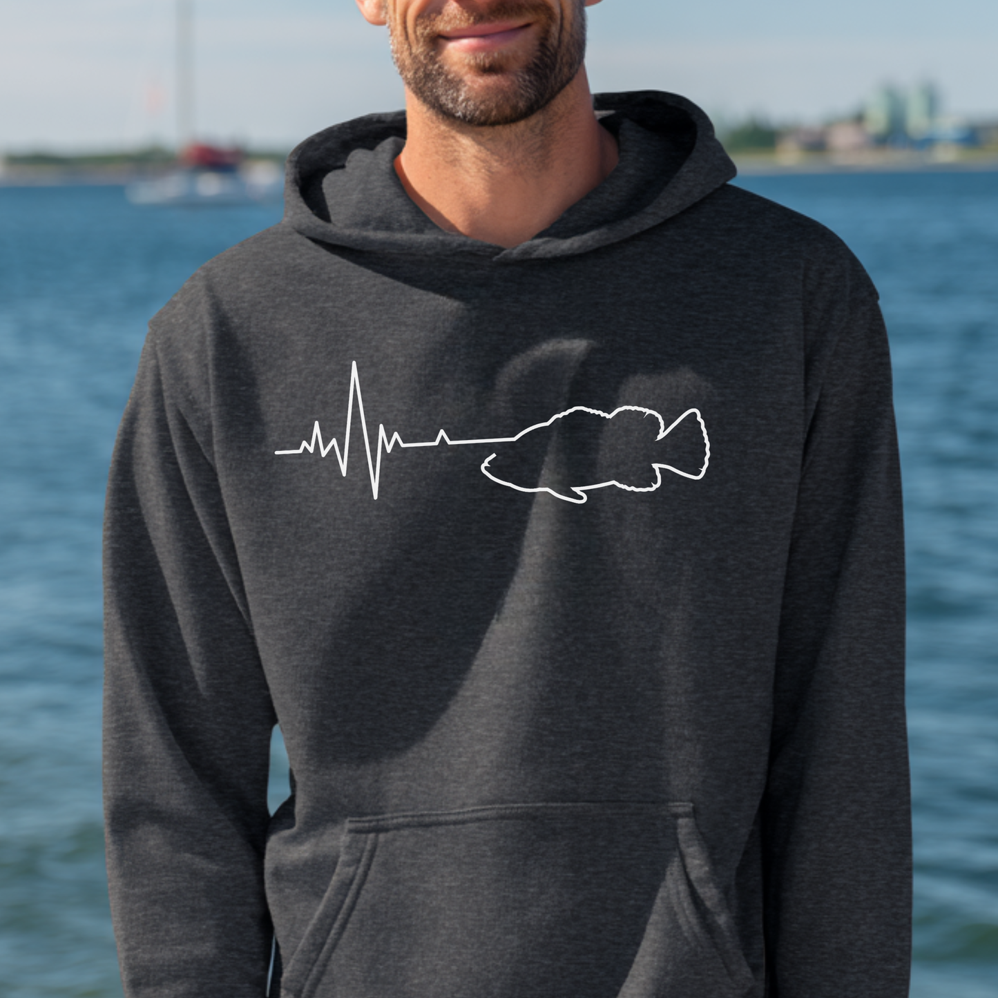 Man wearing a dark gray hoodie with a white graphic design by a body of water.