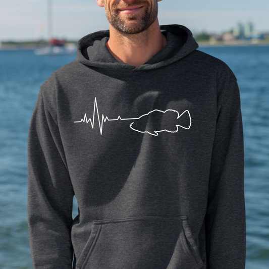Man wearing a dark gray hoodie with a white graphic design by a body of water.