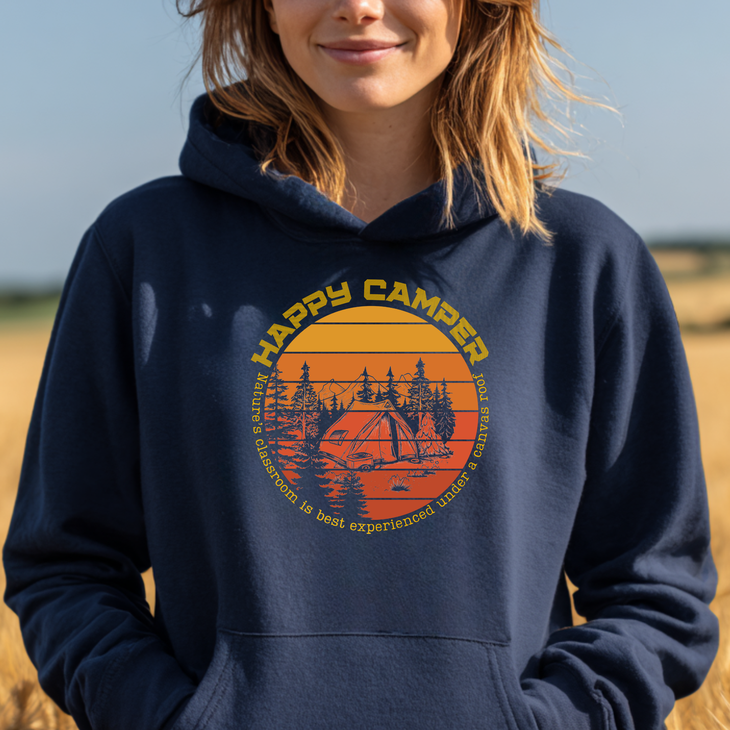 Person wearing a navy blue hoodie with 'Happy Camper' graphic design outdoors.