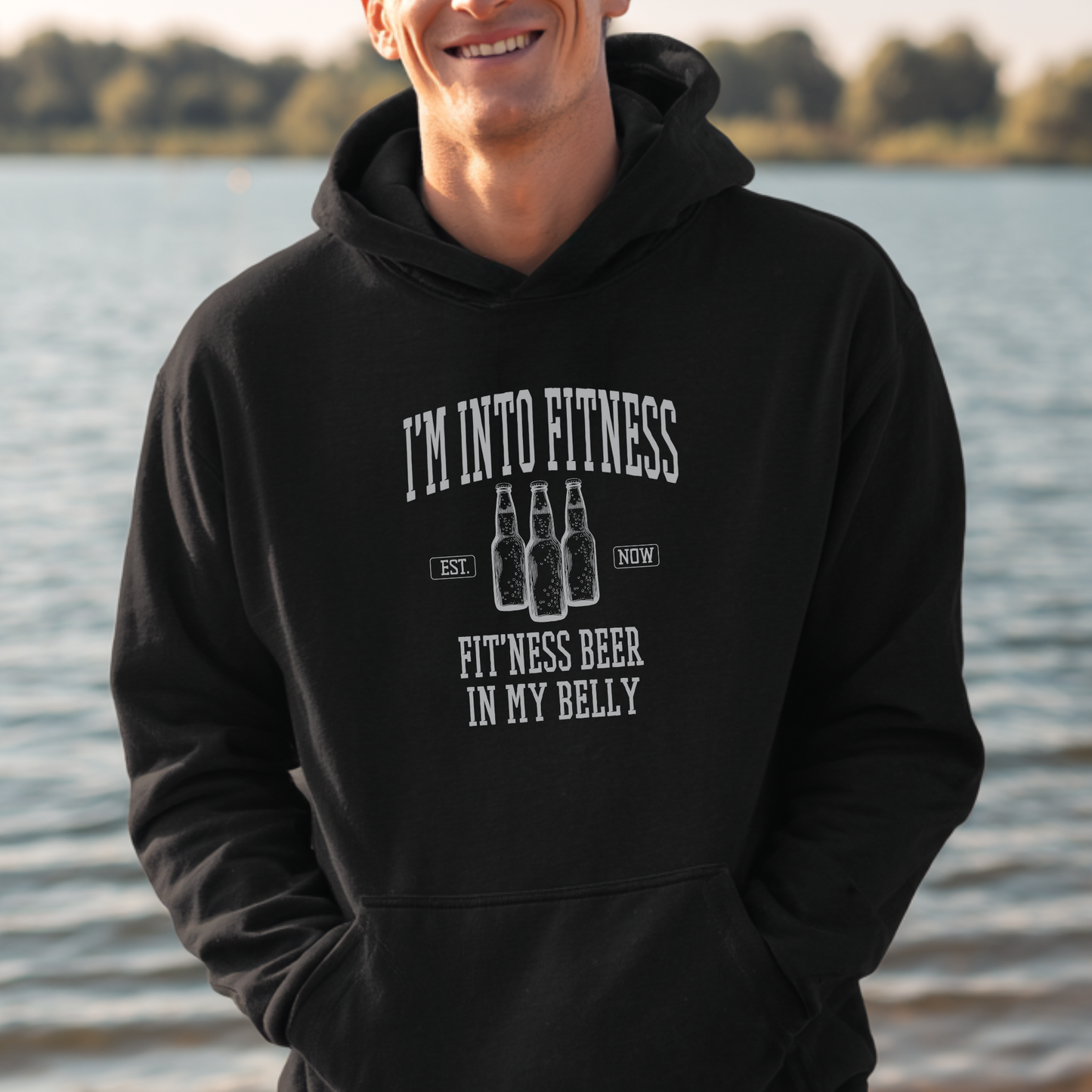 Person wearing a black hoodie with humorous text by a body of water