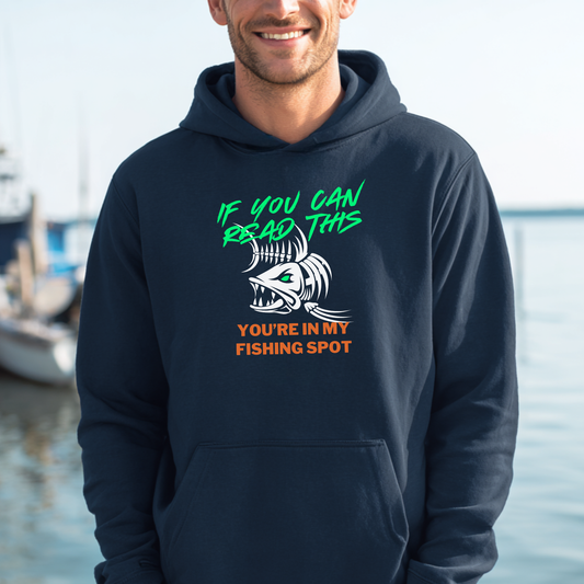 Person wearing a navy hoodie with a humorous fishing graphic and text by a body of water.