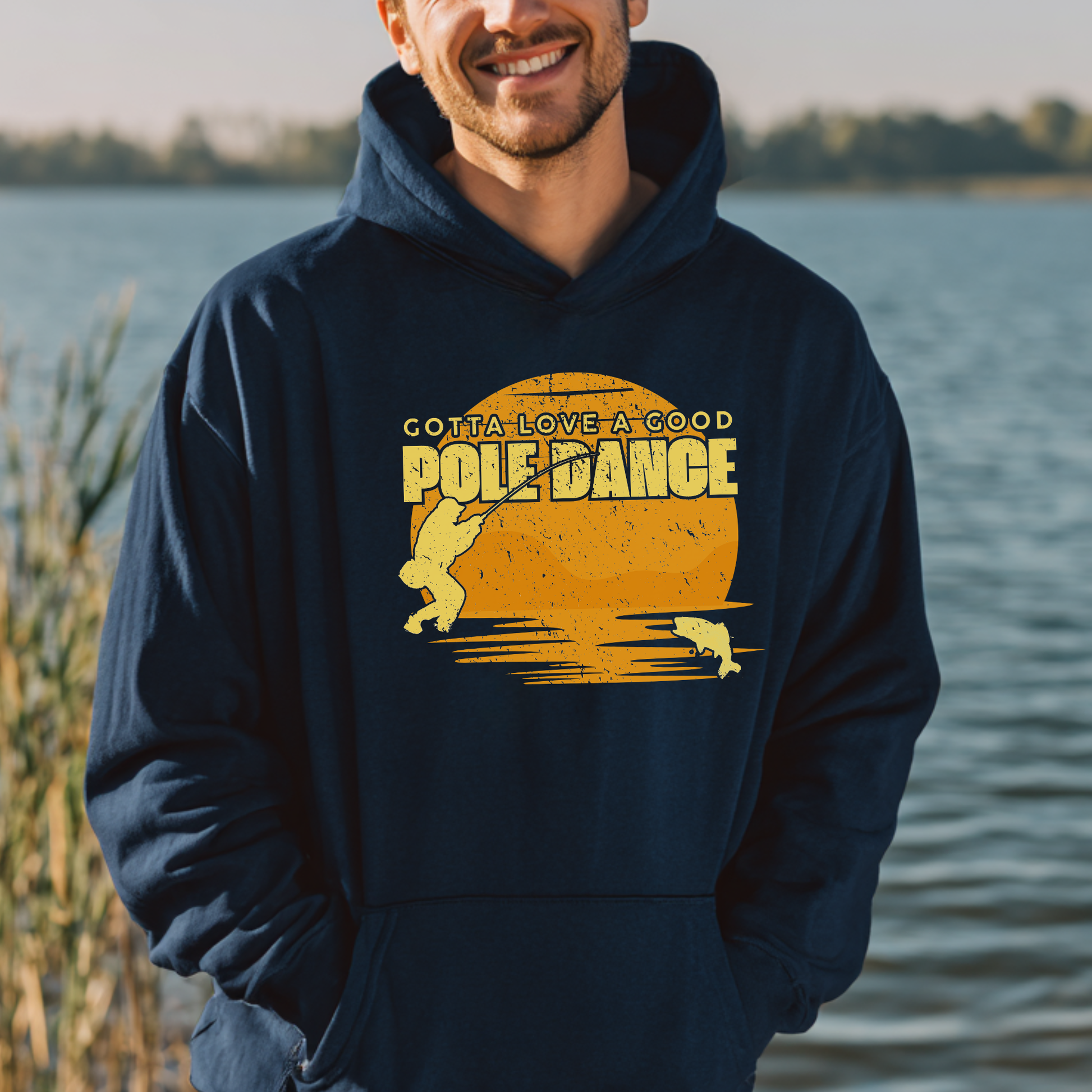Man wearing a navy hoodie with 'Pole Dance' graphic by a body of water