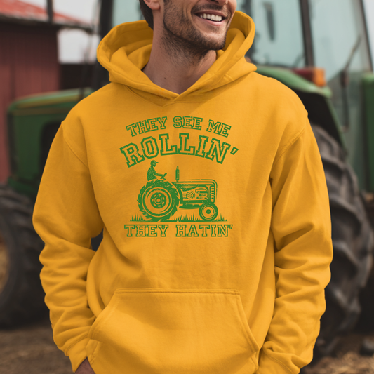 Person wearing a yellow hoodie with a green tractor graphic and text, standing in front of a blurred background with farm equipment.