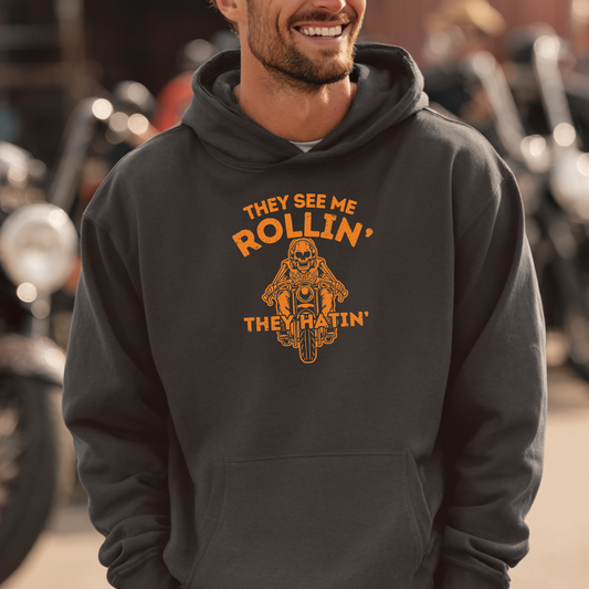 Man wearing a hoodie with a motorcycle graphic and text, standing in front of motorcycles.