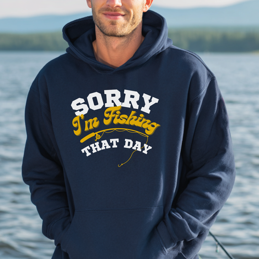 Man wearing a navy hoodie with 'Sorry I'm Fishing That Day' text by a lake.