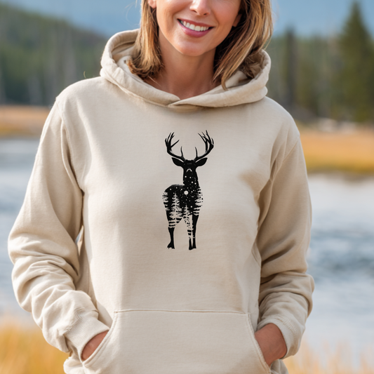 Person wearing a beige hoodie with a black deer design outdoors by a body of water.
