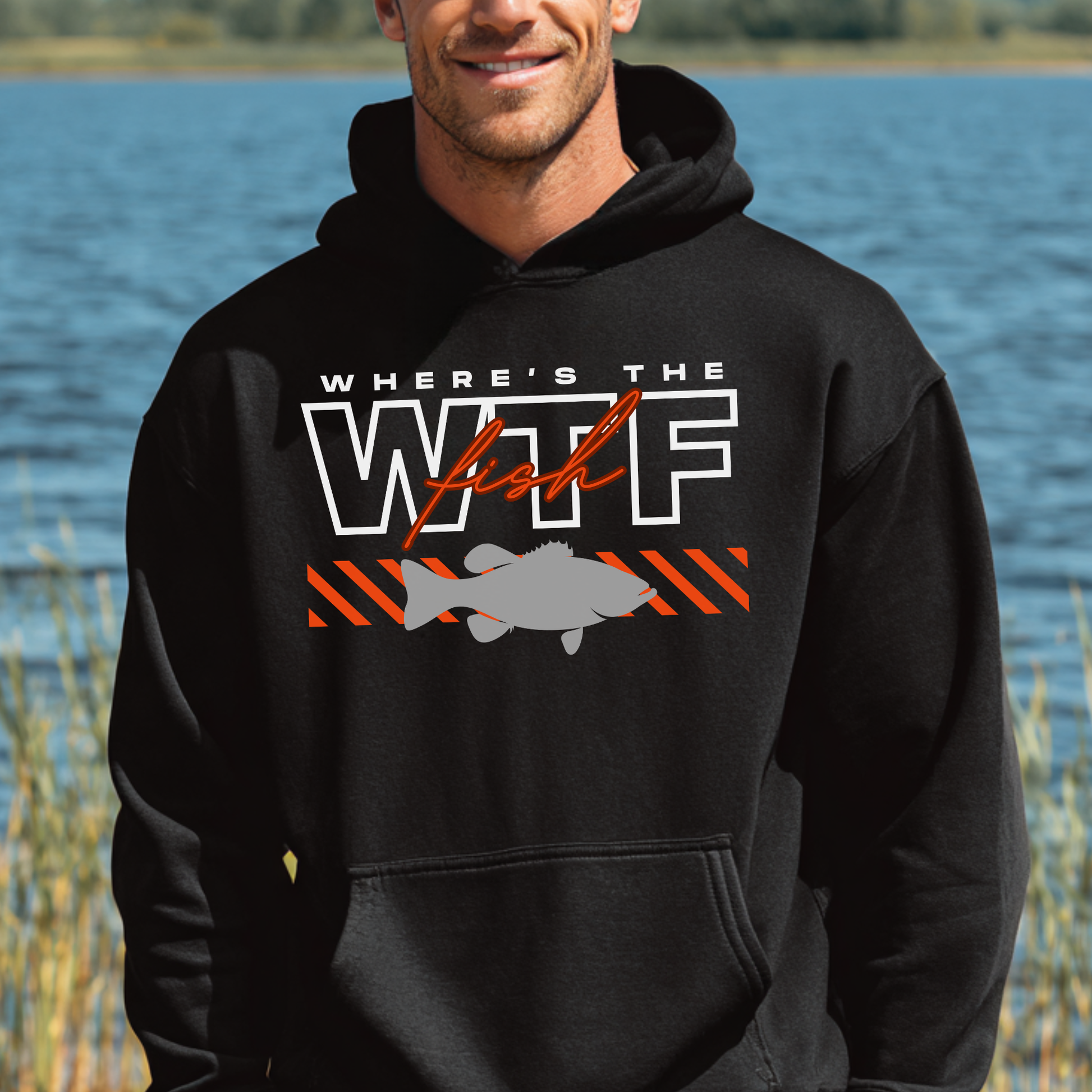 Person wearing a black hoodie with a fish graphic and text by a body of water.