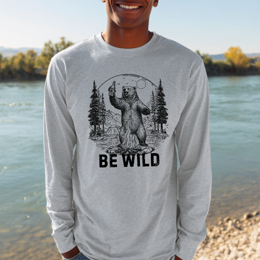 Person wearing a gray long-sleeve shirt with a bear graphic and 'BE WILD' text, standing by a body of water.
