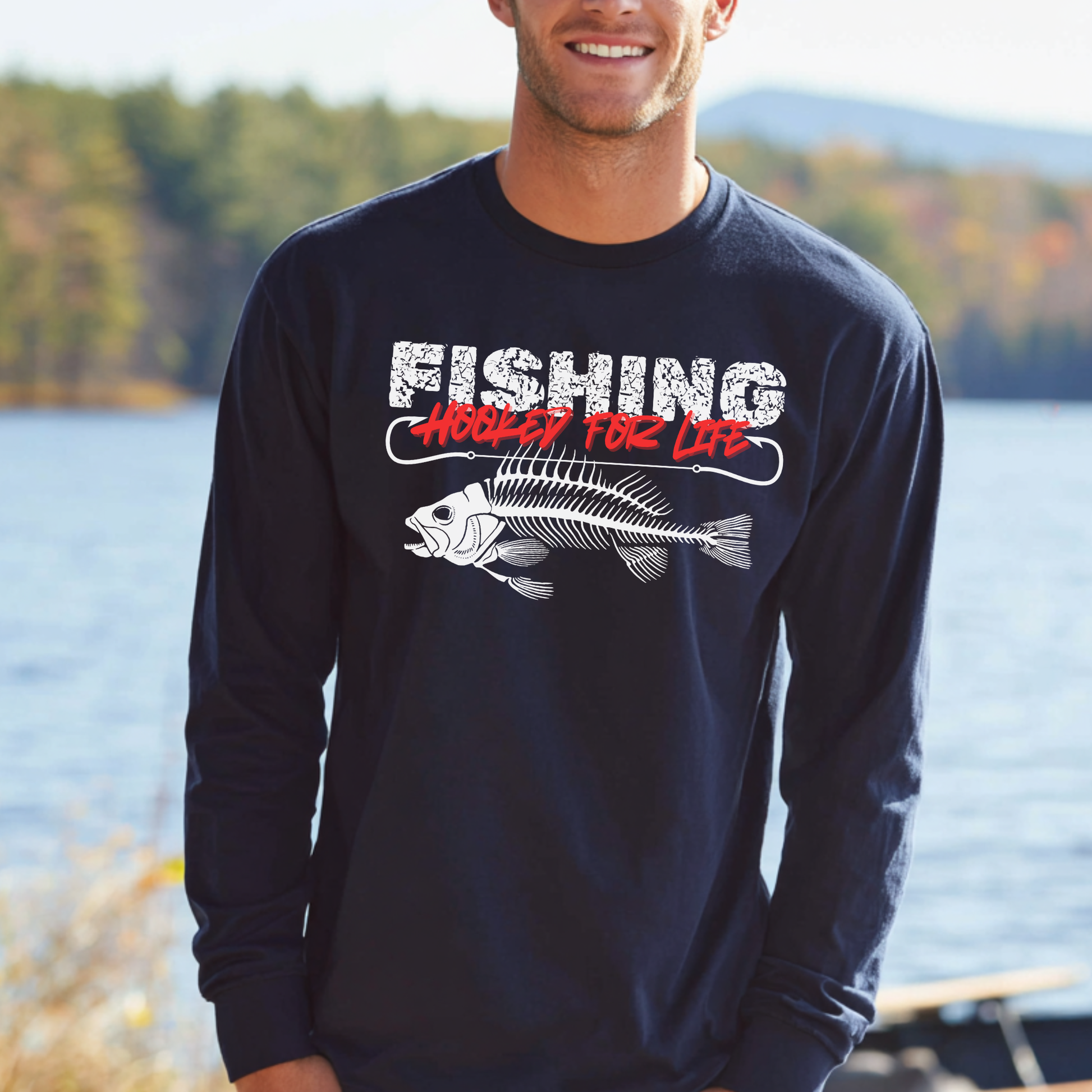 Man wearing a black long-sleeve shirt with a fishing graphic and text by a lake.