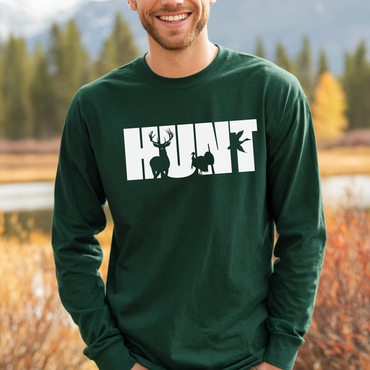 Man wearing a green long-sleeve shirt with 'HUNT' printed on it, standing outdoors with trees and mountains in the background.