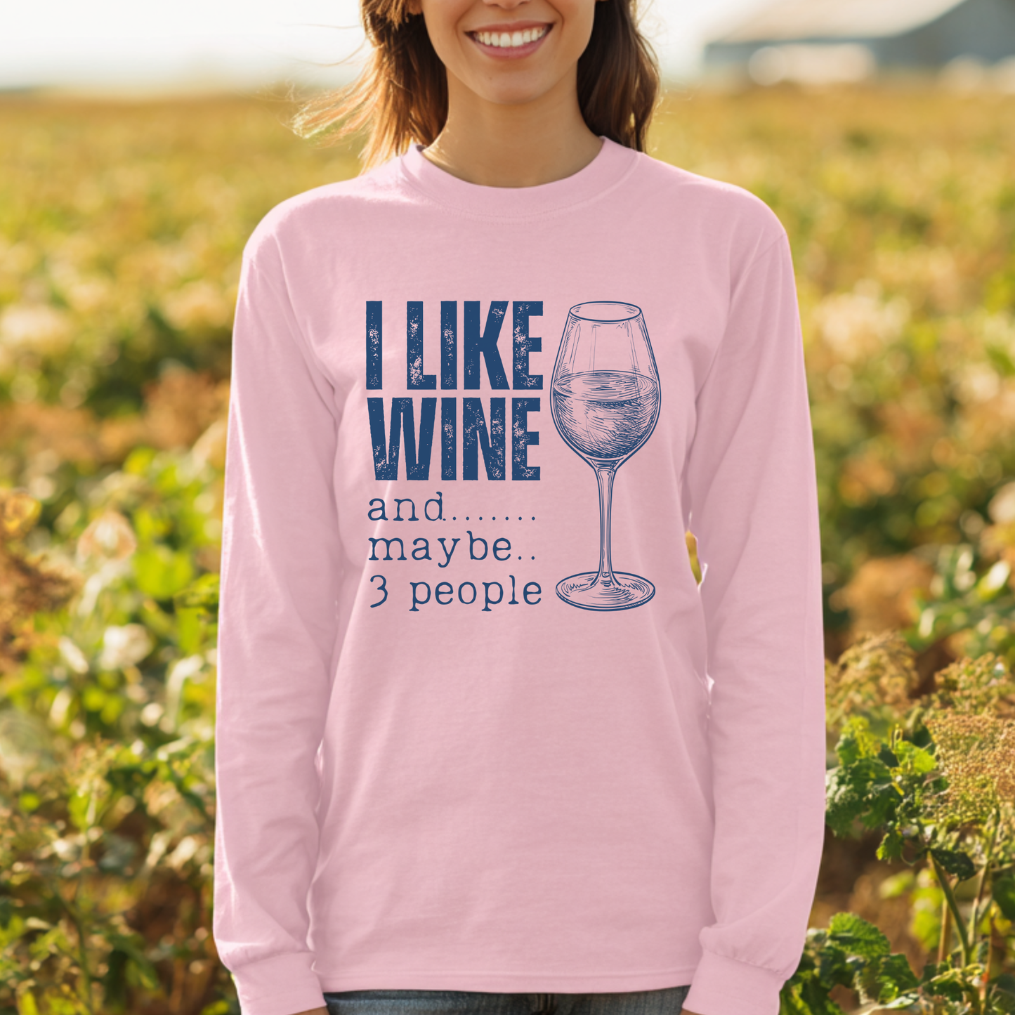 Person wearing a pink long-sleeve shirt with a wine-themed design in a field.