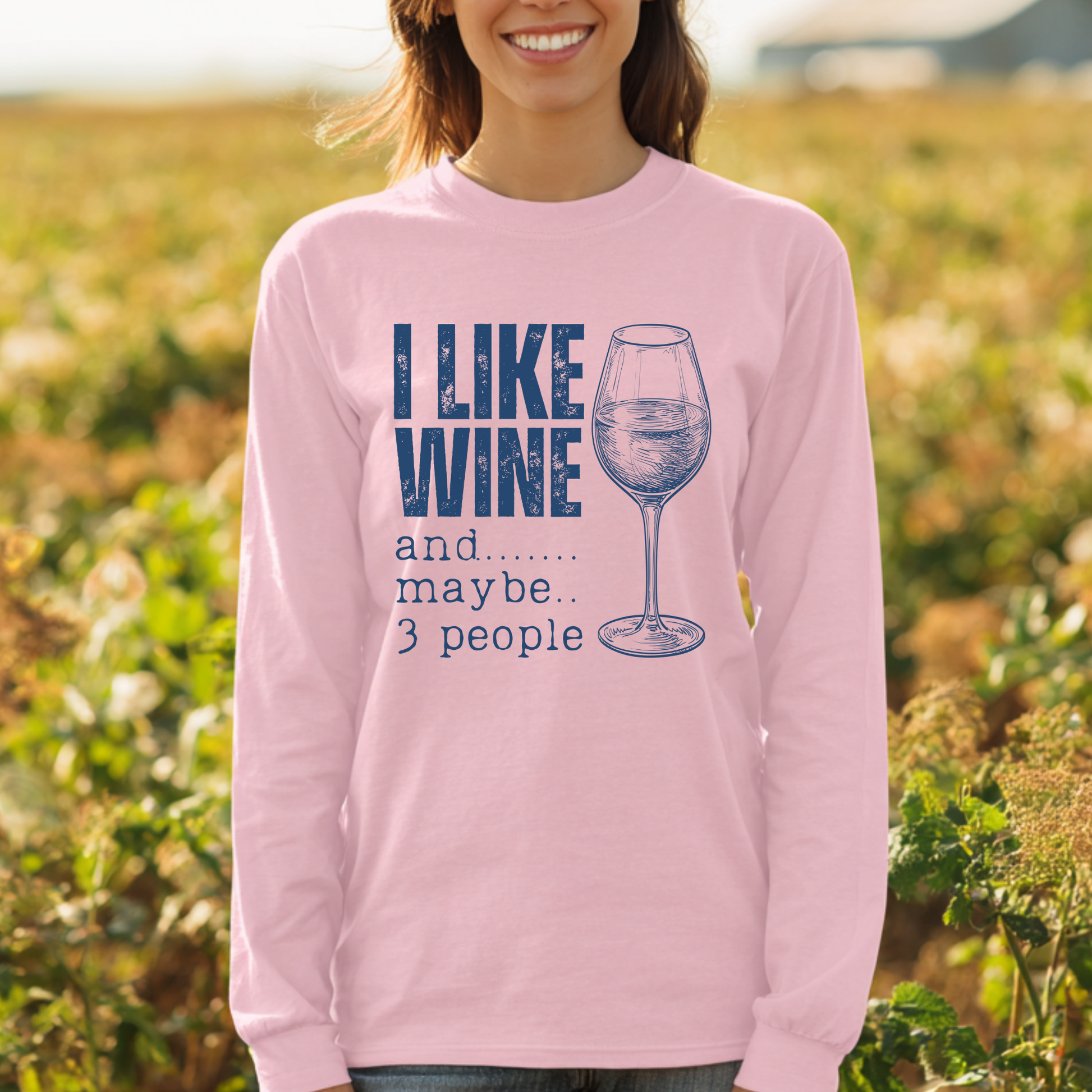 Person wearing a pink long-sleeve shirt with a wine-themed design in a field.