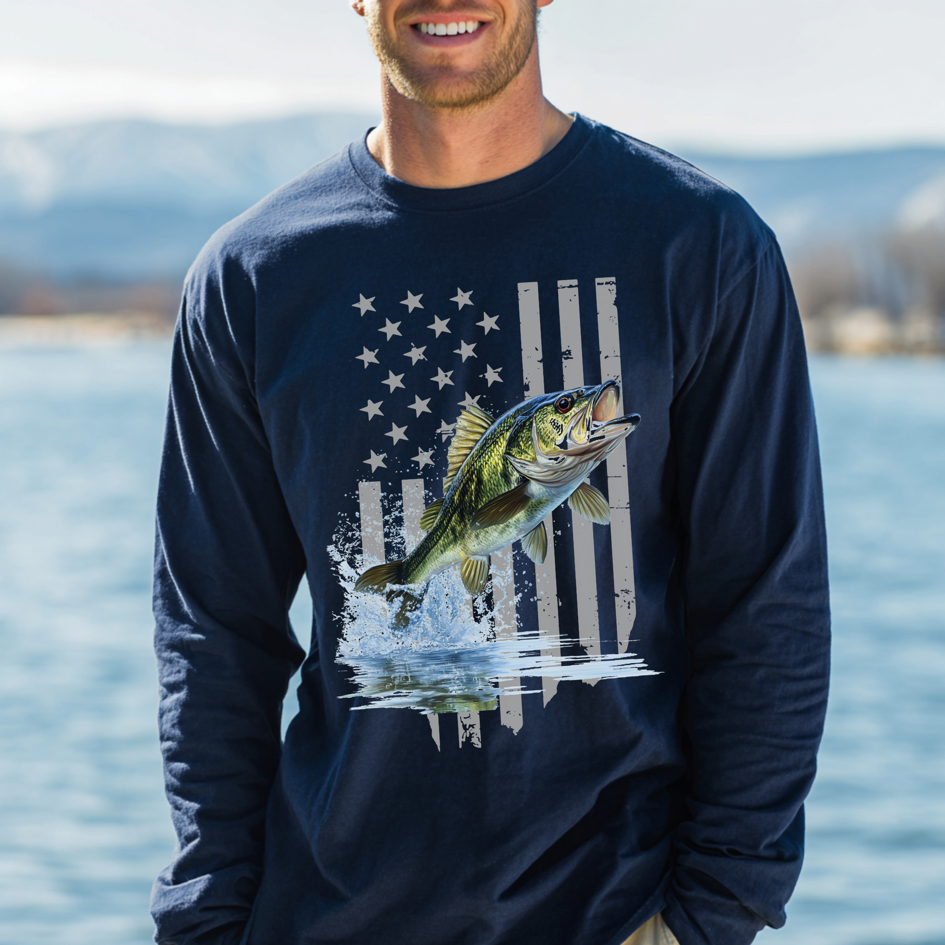 Man wearing a navy blue long-sleeve shirt with a fish and American flag design, standing by a body of water.