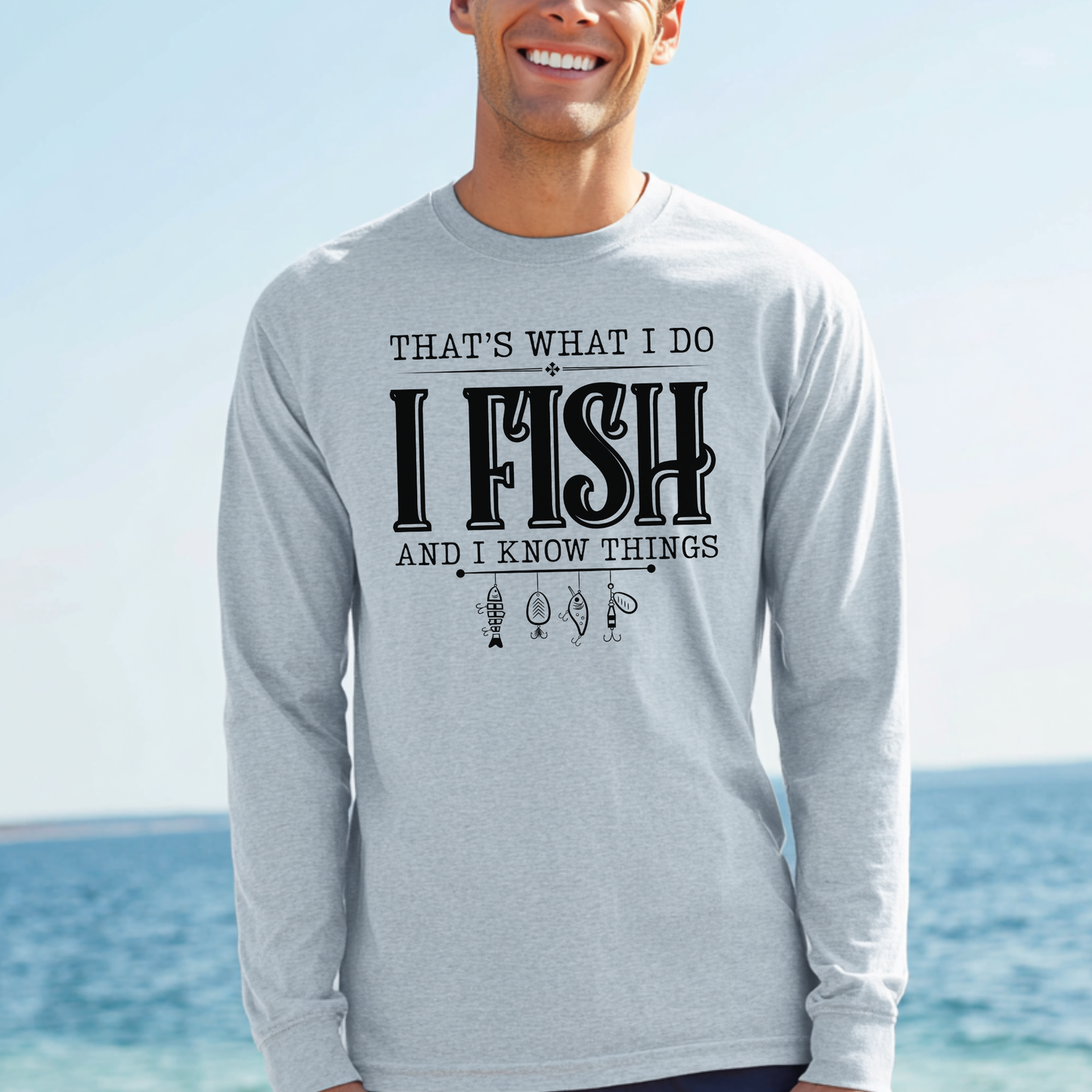 Man wearing a gray long-sleeve shirt with fishing-themed text by the ocean.