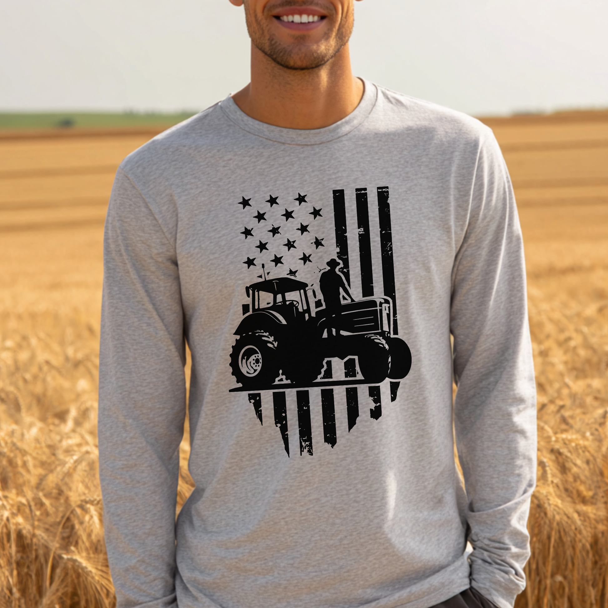 Person wearing a gray long-sleeve shirt with a tractor and flag design in a field.