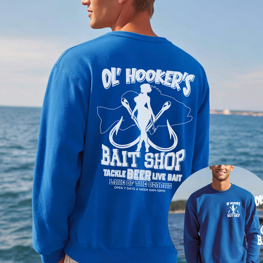 Person wearing a blue sweatshirt with 'Ol' Hooker's Bait Shop' design by the ocean.