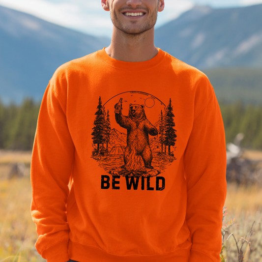Person wearing an orange sweatshirt with a bear graphic and 'BE WILD' text, standing in a natural setting.