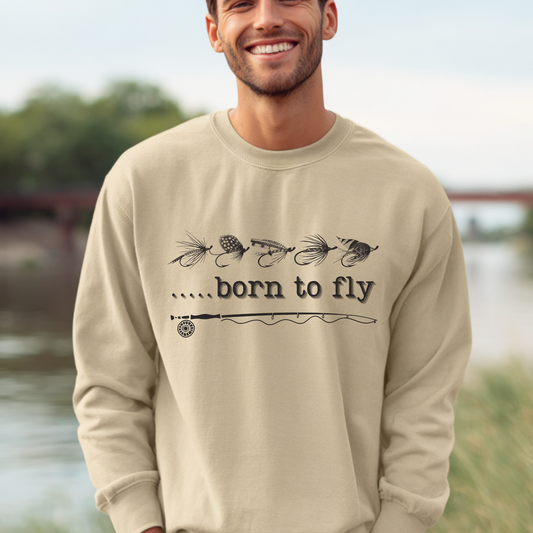 Man wearing a beige sweatshirt with 'born to fly' text and fishing lure graphics outdoors.