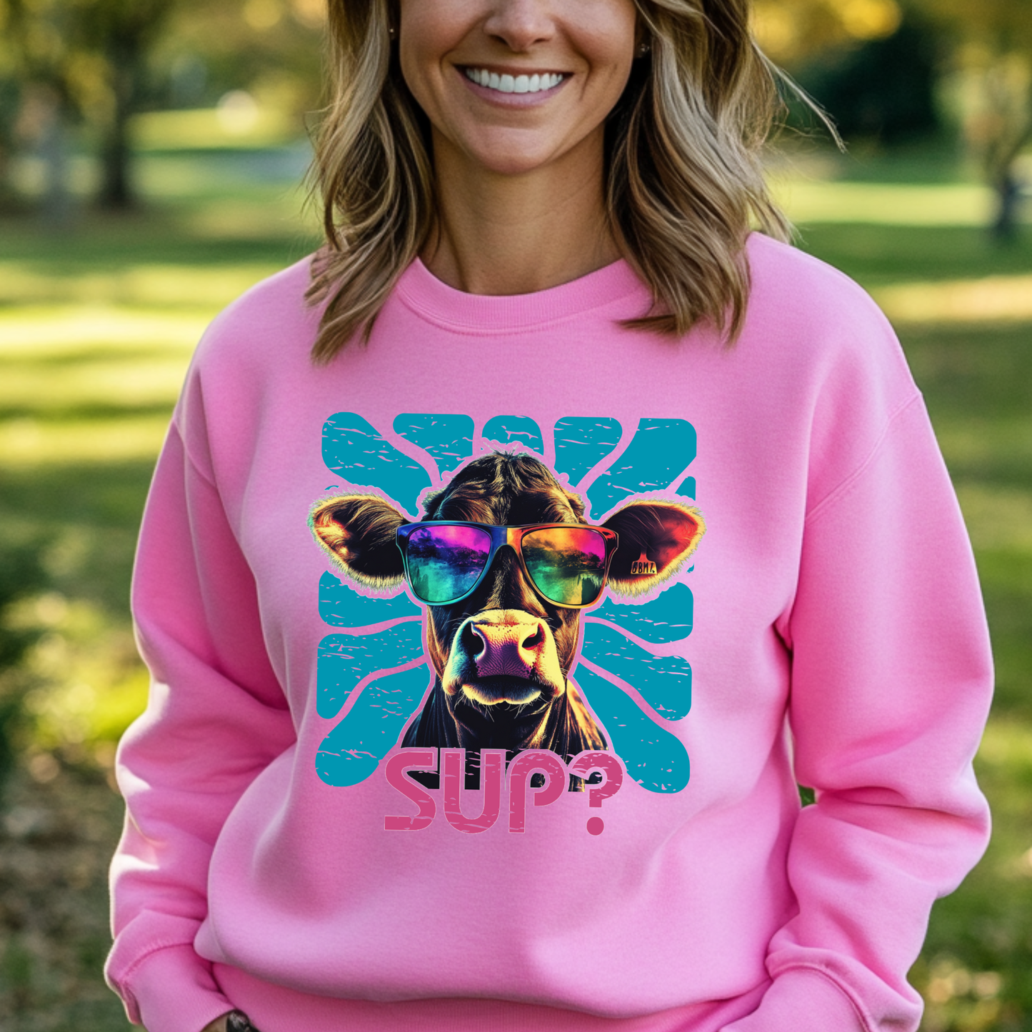 Person wearing a pink sweatshirt with a cow graphic and 'SUP?' text outdoors.