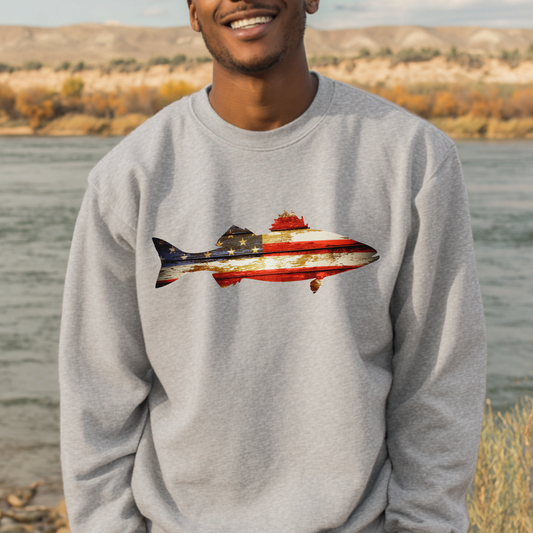 Person wearing a gray sweatshirt with a fish design featuring the American flag, standing by a body of water.