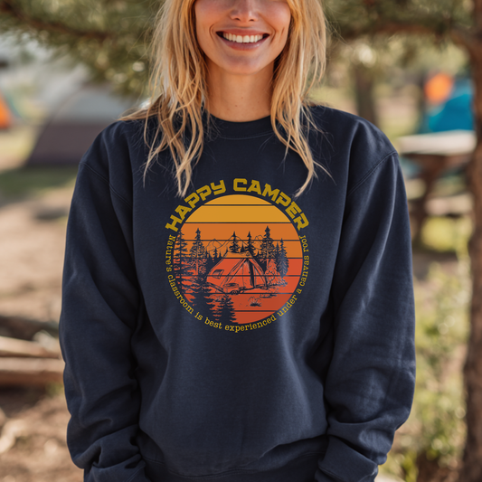 Person wearing a navy blue sweatshirt with 'Happy Camper' graphic in a forest setting