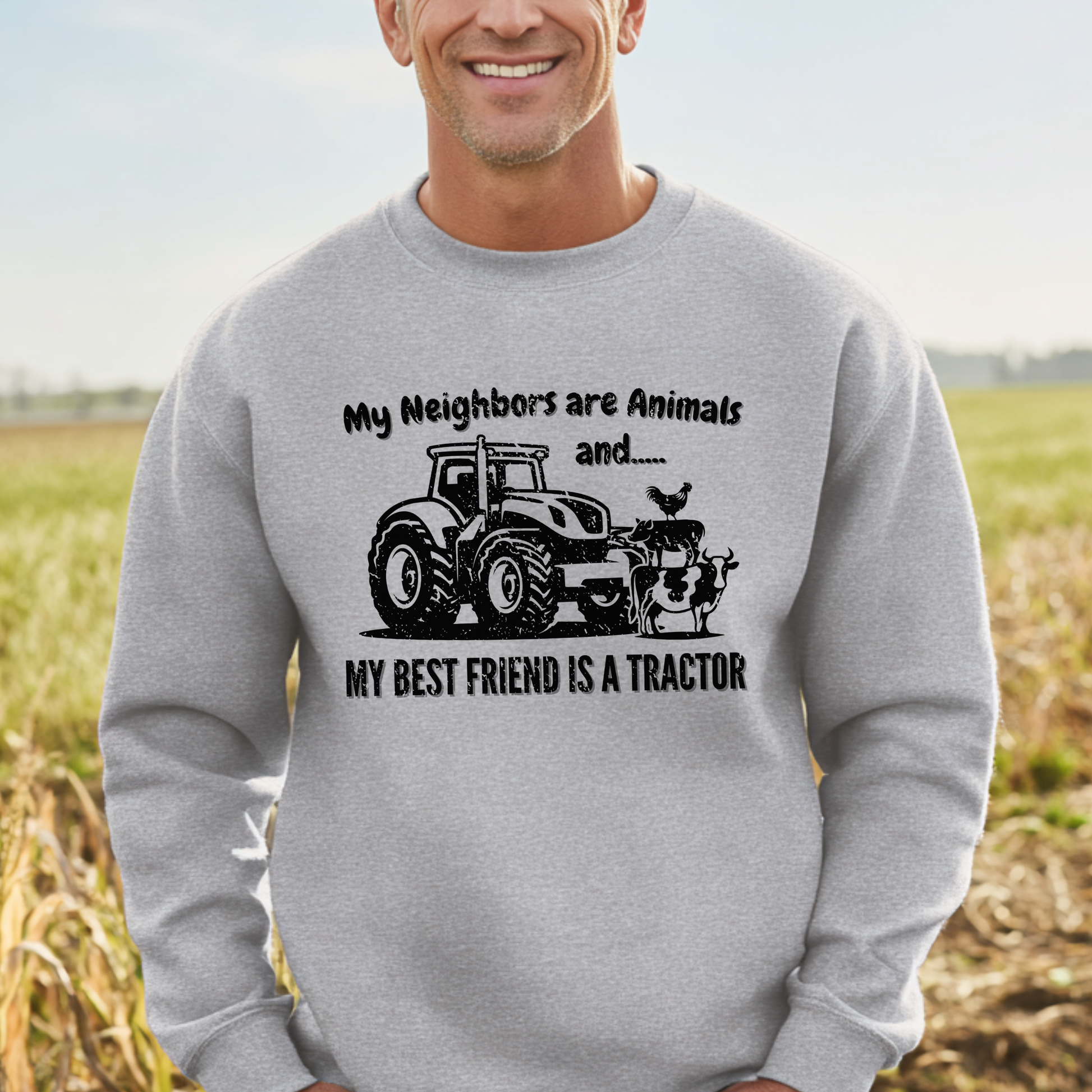 Man wearing a gray sweatshirt with a tractor graphic and text in a field.
