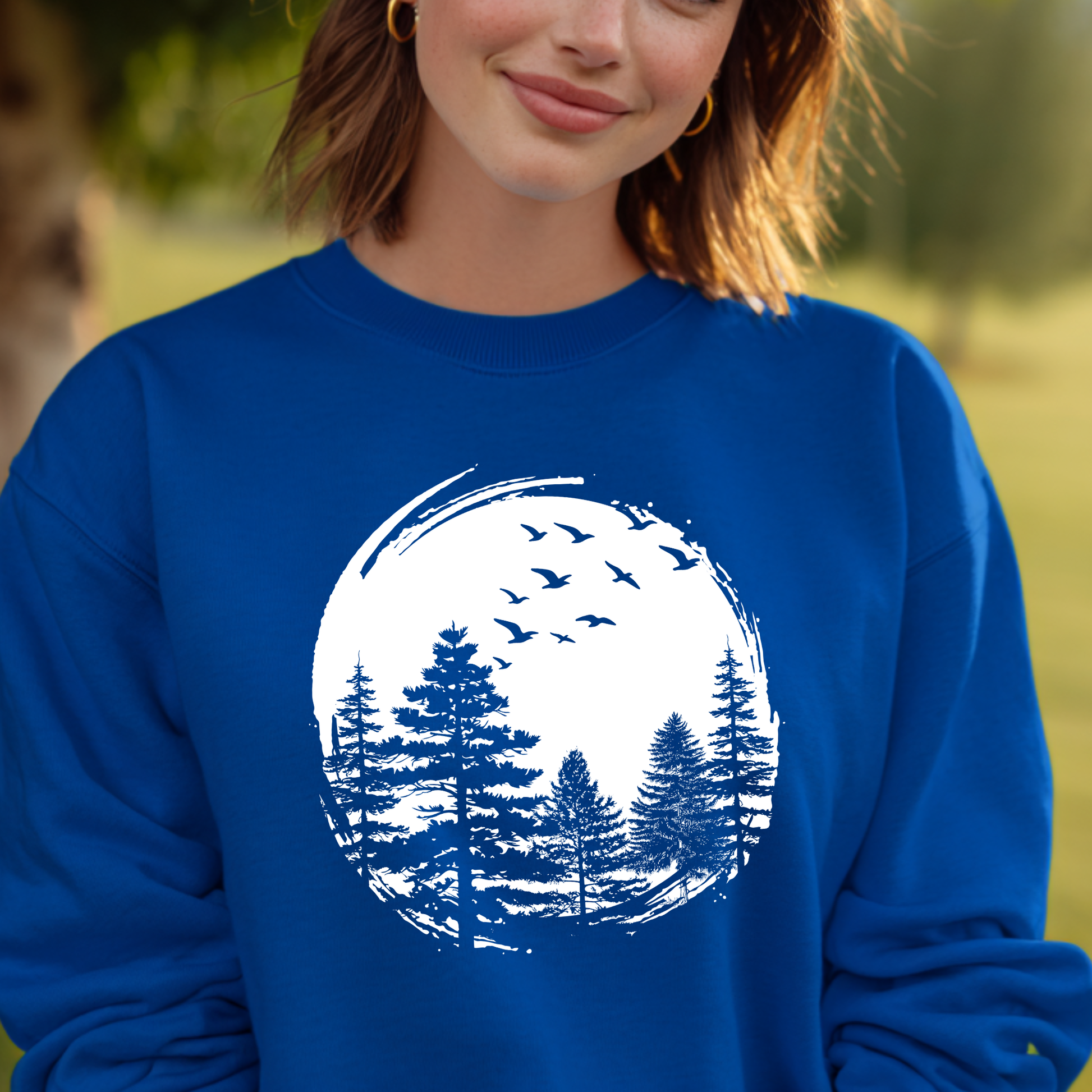 Person wearing a blue sweatshirt with a white nature graphic of trees and birds.