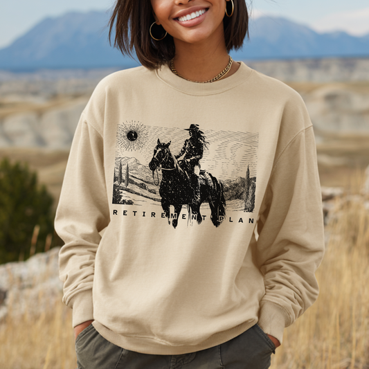 Person wearing a beige sweatshirt with a horse and rider graphic and 'Retirement Plan' text, standing in a scenic outdoor setting.