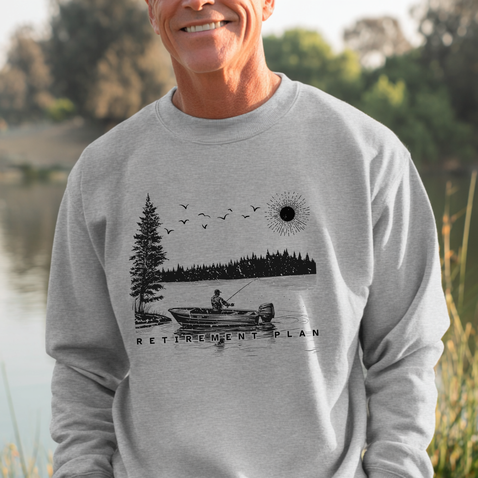 Man wearing a gray sweatshirt with a fishing graphic and 'Retirement Plan' text, standing outdoors.