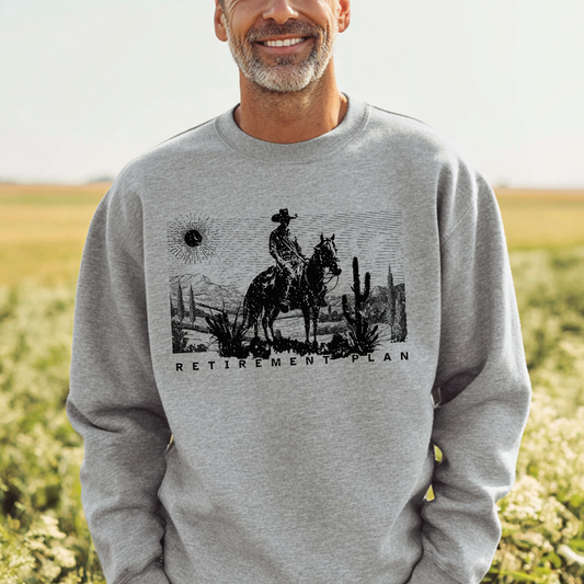 Man wearing a gray sweatshirt with a graphic design of a cowboy on a horse and the text 'Retirement Plan' in a field.