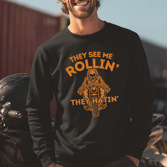 Man wearing a black sweatshirt with a graphic and text, sitting next to a motorcycle.