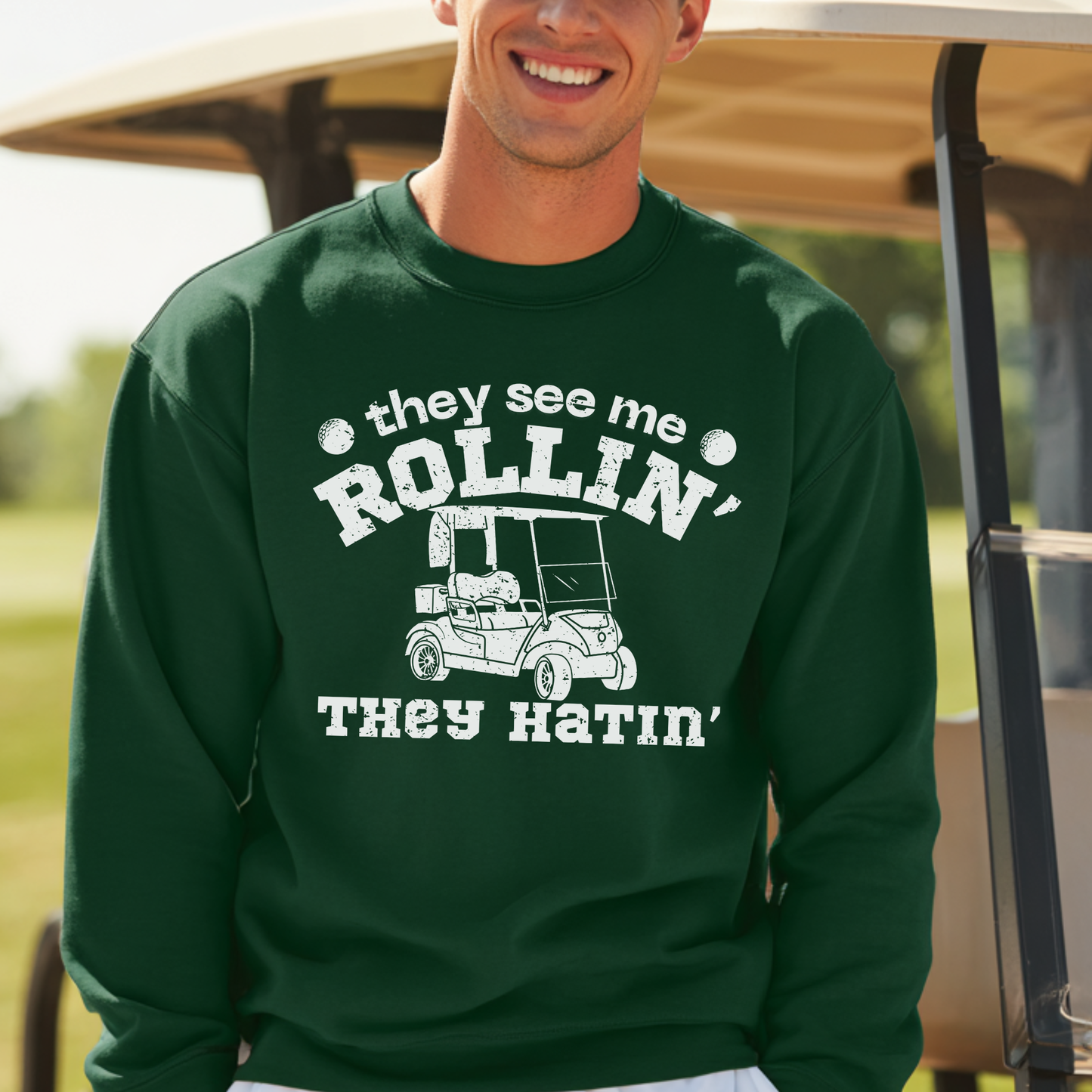 Man wearing a green sweatshirt with a humorous graphic and text, standing in front of a golf cart.