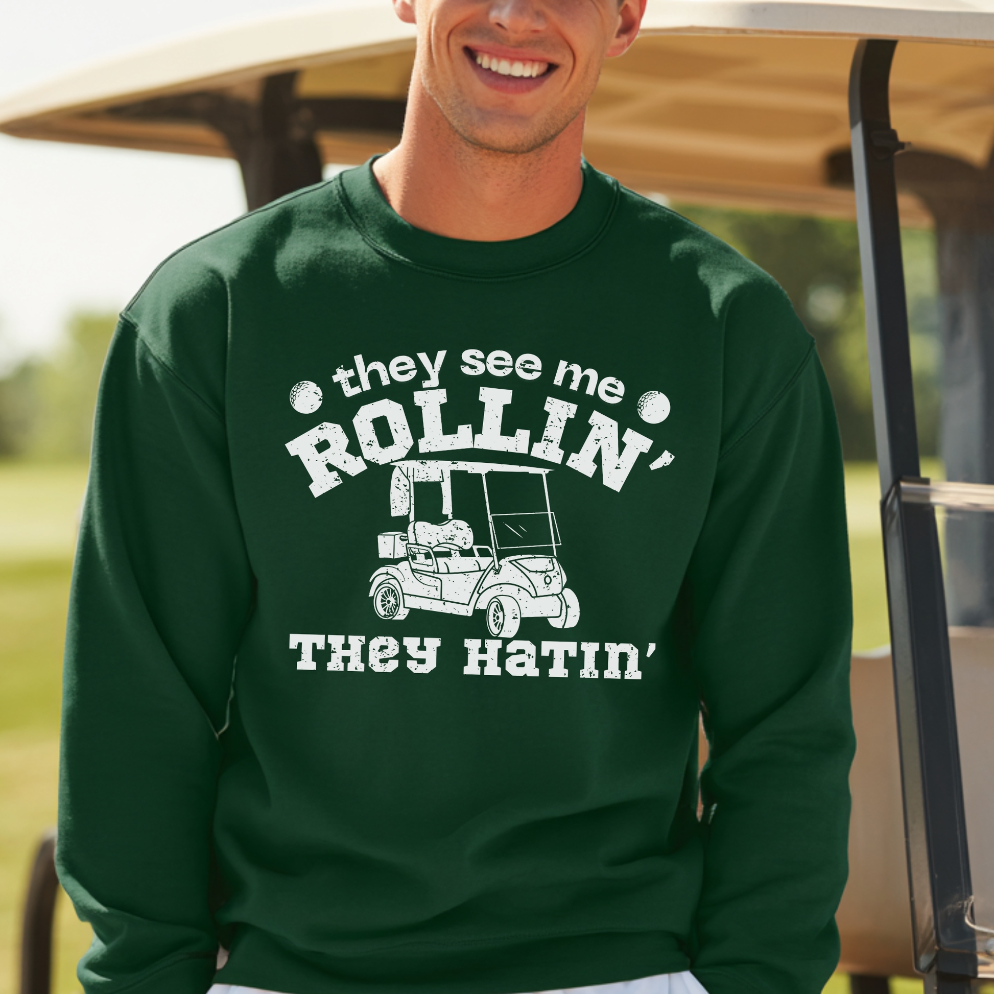 Man wearing a green sweatshirt with a humorous graphic and text, standing in front of a golf cart.