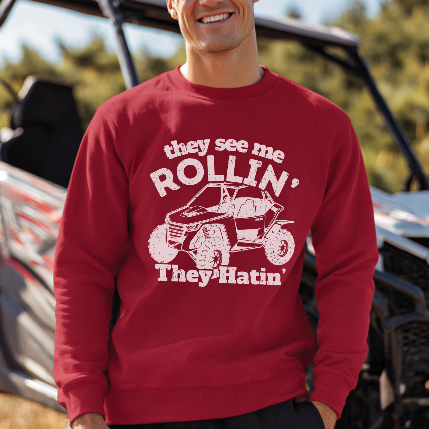 Person wearing a red sweatshirt with a graphic and text in front of an off-road vehicle.