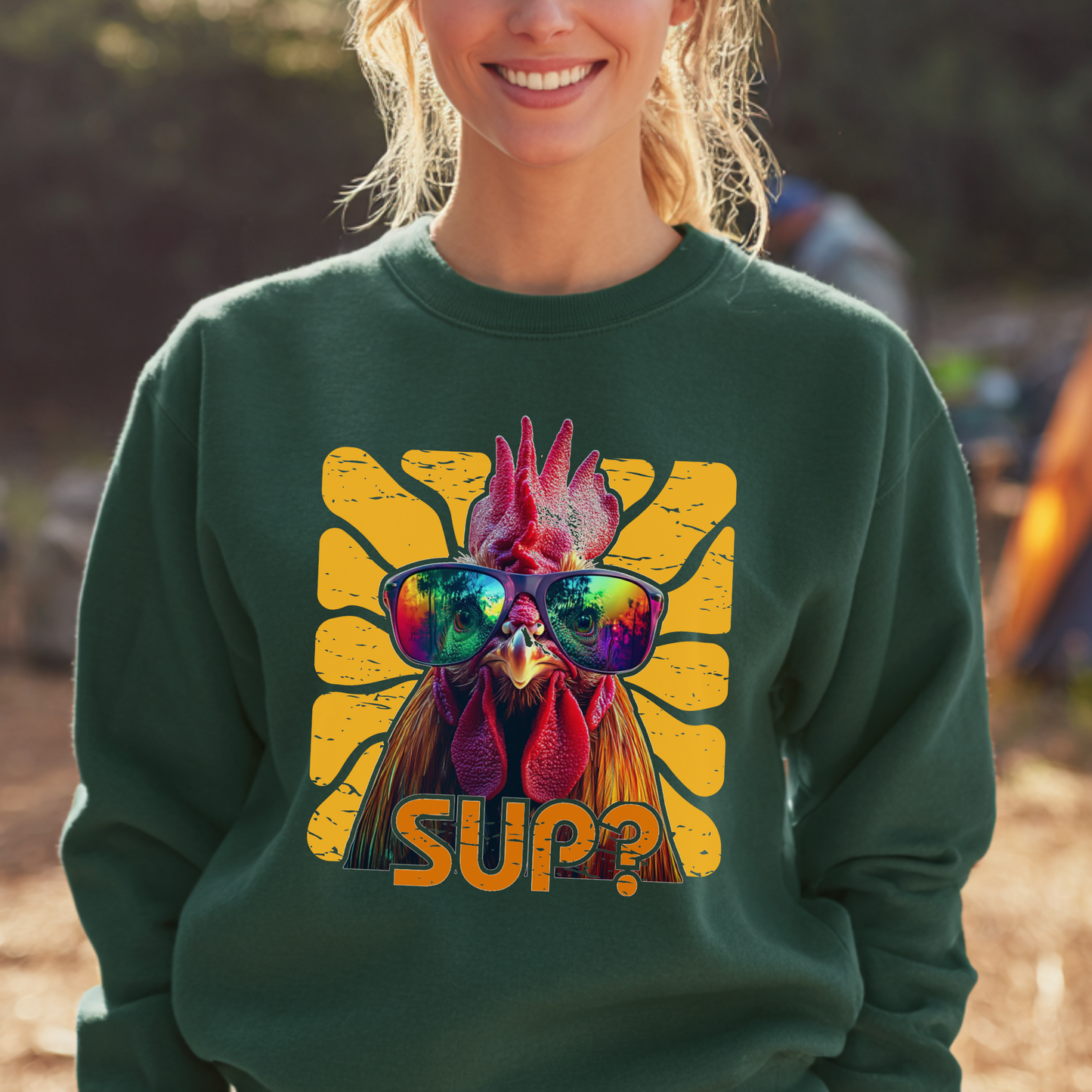 Person wearing a green sweatshirt with a rooster graphic and 'SUP?' text outdoors.