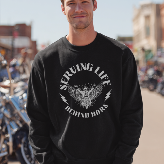 Man wearing a black sweatshirt with a graphic design and text, standing in an outdoor setting with motorcycles.