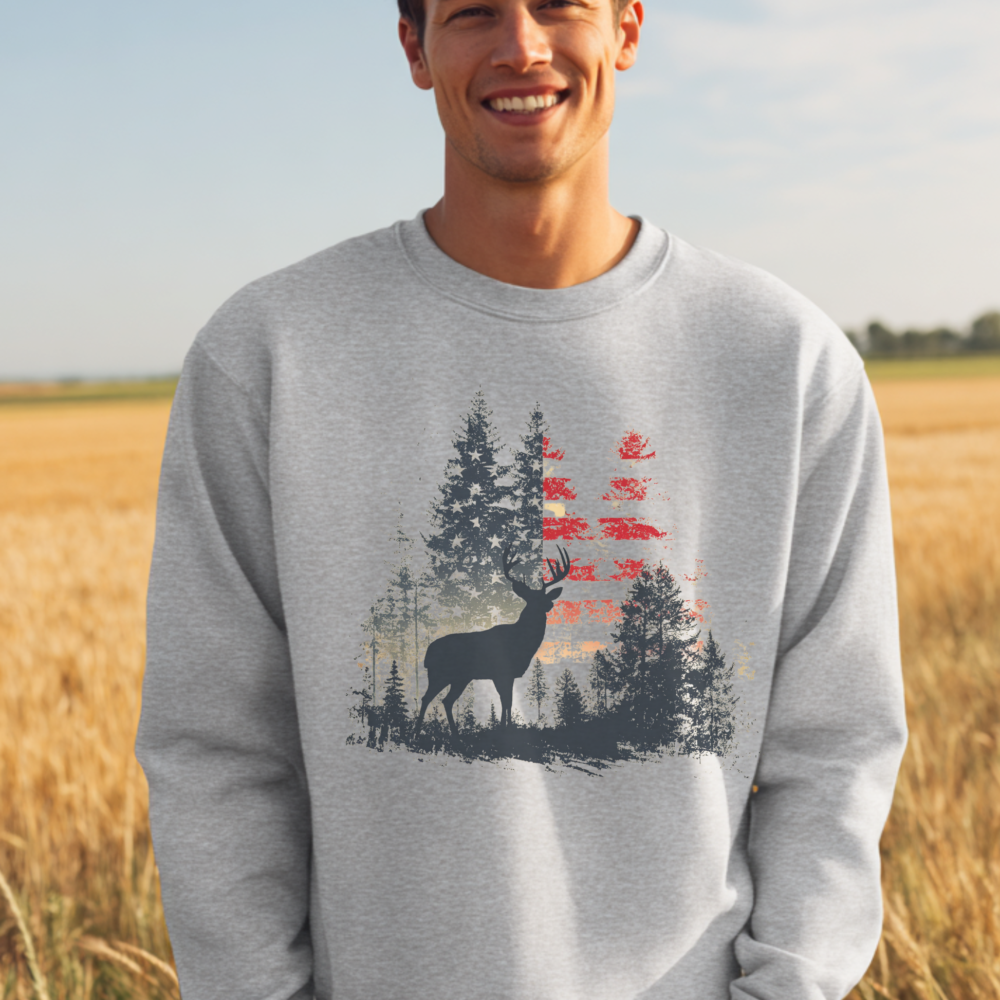 Man wearing a gray sweatshirt with a deer and forest design, standing in a field.