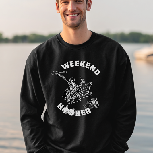 Man wearing a black sweatshirt with 'Weekend Hooker' graphic by a body of water.