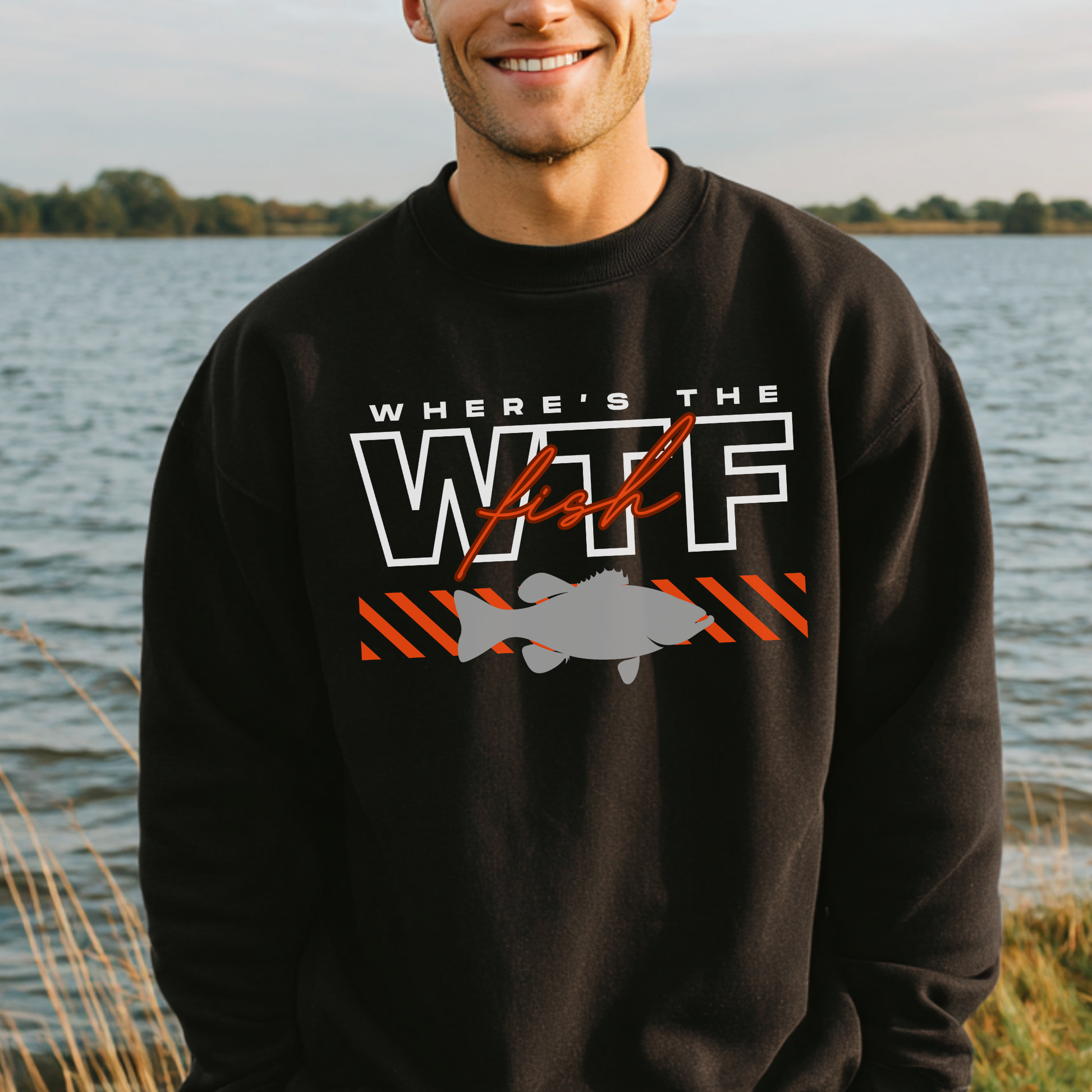 Man wearing a black sweatshirt with a fishing-themed design by a lake.