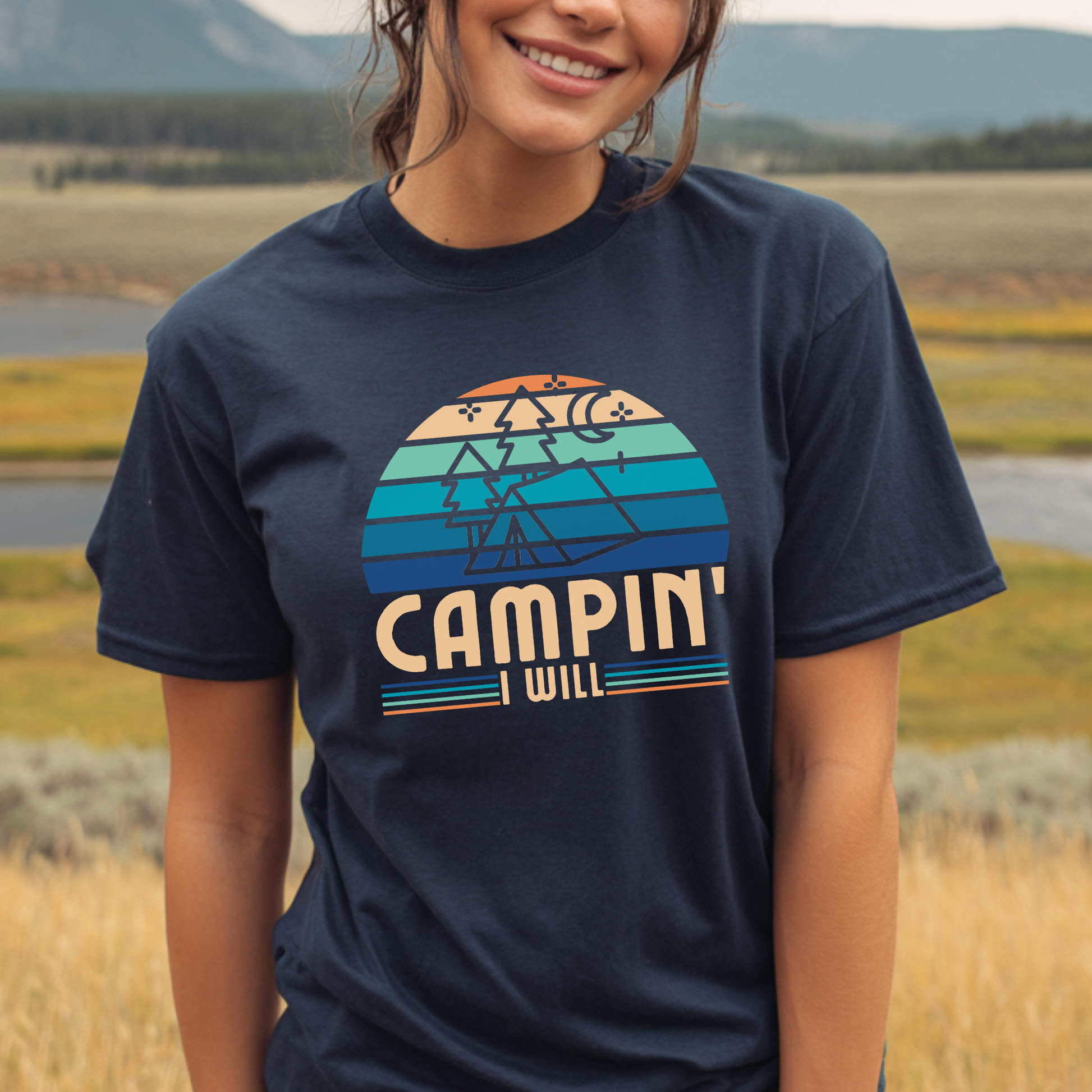 Person wearing a navy blue t-shirt with 'CAMPIN' I WILL' graphic design outdoors.