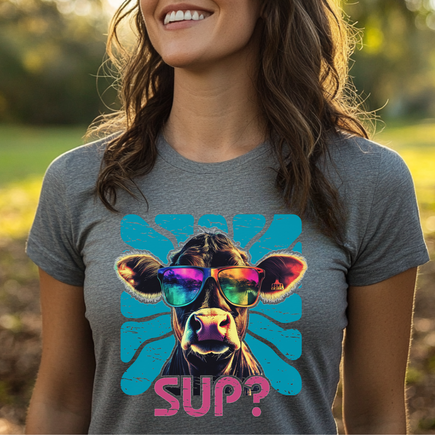 Person wearing a gray t-shirt with a cow graphic and 'SUP?' text outdoors.