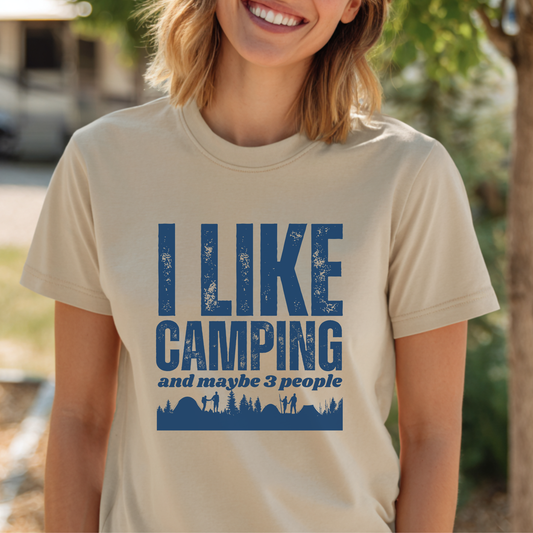 Person wearing a beige t-shirt with blue text 'I LIKE CAMPING and maybe 3 people' in an outdoor setting.