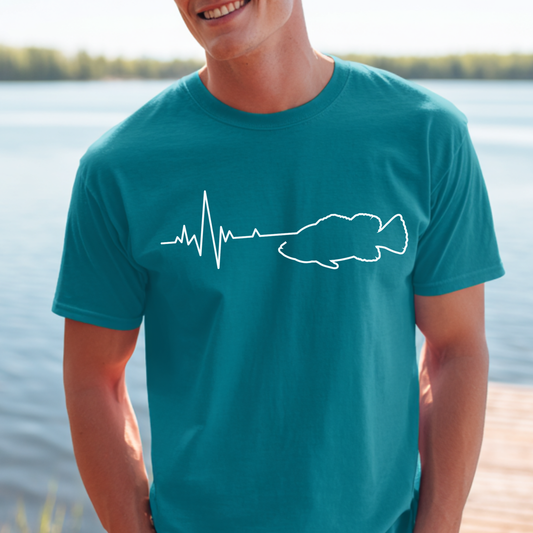 Person wearing a teal t-shirt with a white graphic design by a body of water.