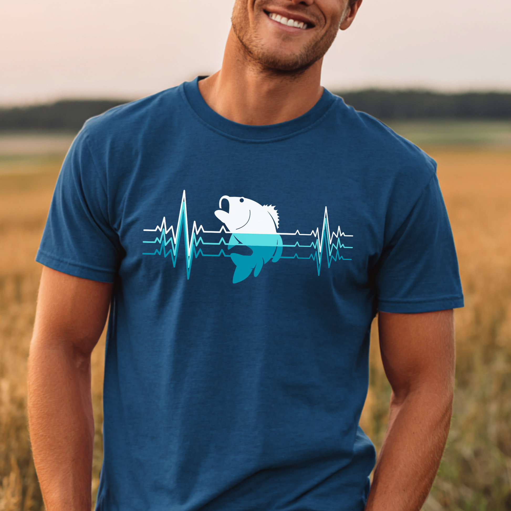 Man wearing a blue t-shirt with a graphic design of a fish and heartbeat lines, standing in a field.