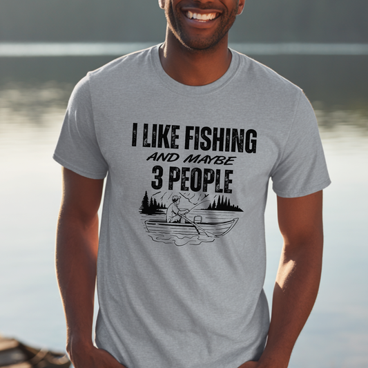 Man wearing a gray t-shirt with a fishing graphic and text by a body of water.